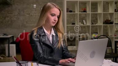 白种人金发<strong>认真工</strong>作的女孩，坐在砖头办公室，在桌面上使用她的电脑的录像